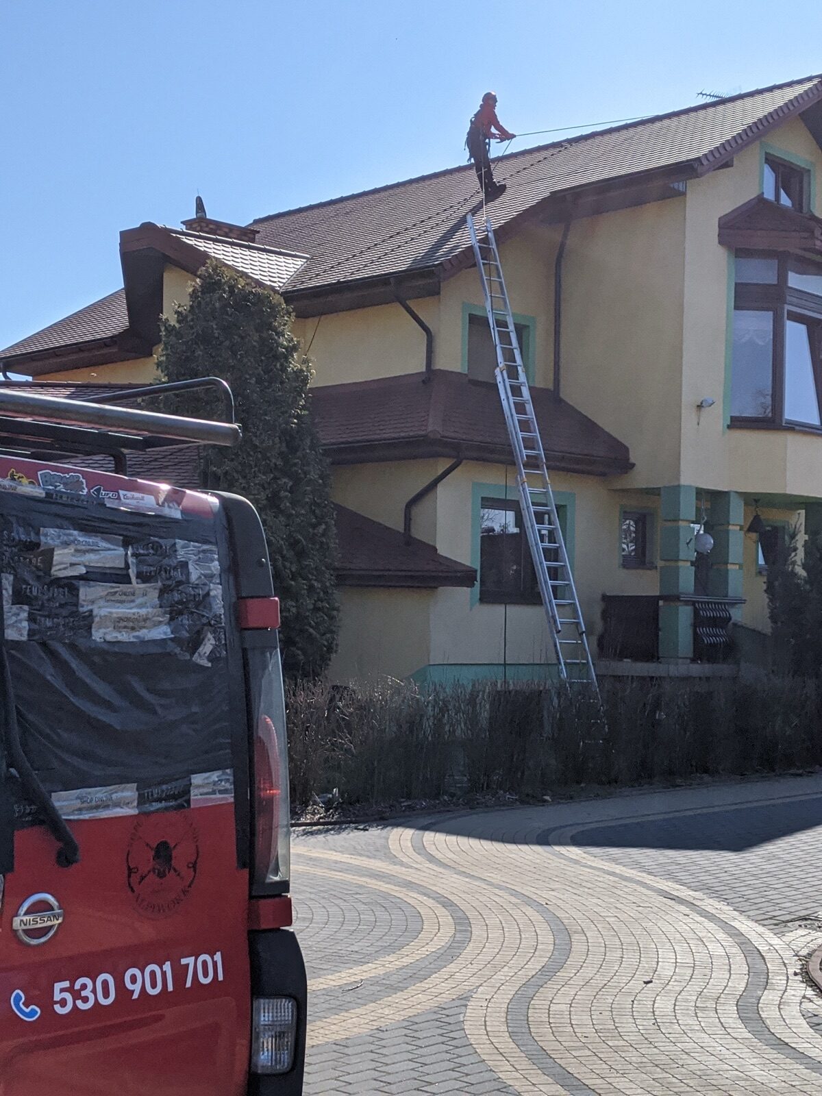 Alpinista Alpiwork na linie myje dach domu jednorodzinnego, przed domem bus firmy z numerem 530 901 701
